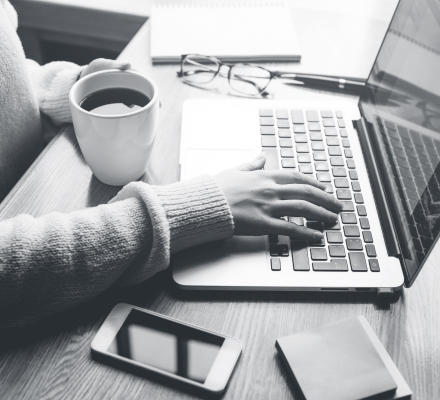 Woman working at desk with coffee, phone and laptop